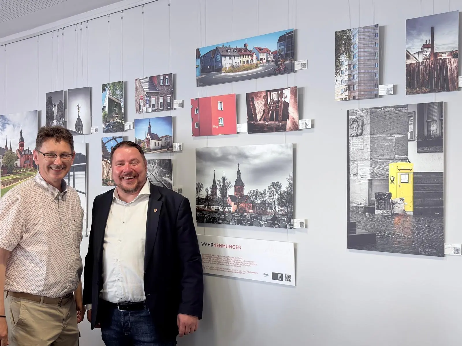 Hobbyfotograf Dirk Schneider und Erster Stadtrat Oliver Steidl stehen vor Fotografien im Nachbarschaftshaus.