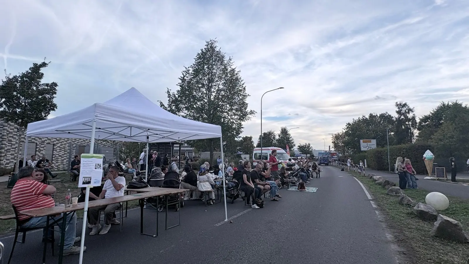 Besucherinnen und Besucher sitzen an Tischen auf der Straße beim Stadtteilfest rund um das Nachbarschaftshaus.