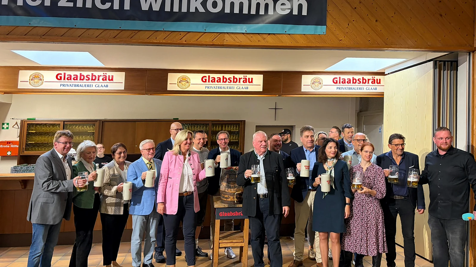 Eine Gruppe von Festgästen steht mit Gläsern und Bierkrügen vor dem Ausschank im Bürgerhaus.