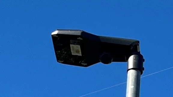 Schwarzer LED-Leuchtenkopf an einem verzinkten Mast vor blauem Himmel.