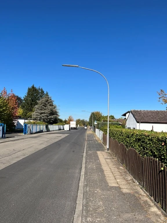 Straßenlaterne an einer Wohnstraße mit Gehweg, Hecken und Häusern.